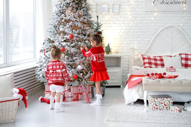 Les filles décorent le sapin de Noël dans la chambre à coucher en accrochant des boules et des jouets en forme de canne en bonbon