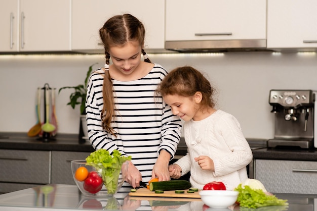 Les filles de deux soeurs mignonnes coupent une salade de légumes frais Nourriture saine Enfance