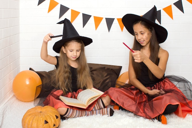 Filles drôles en costumes de sorcières pour faire peur à Halloween à l'aide d'un livre magique