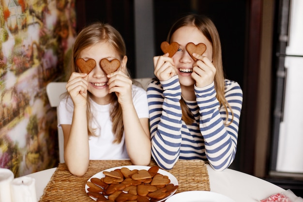 Des filles drôles et rieuses tiennent des biscuits en forme de cœur, ferment les yeux et s'amusent