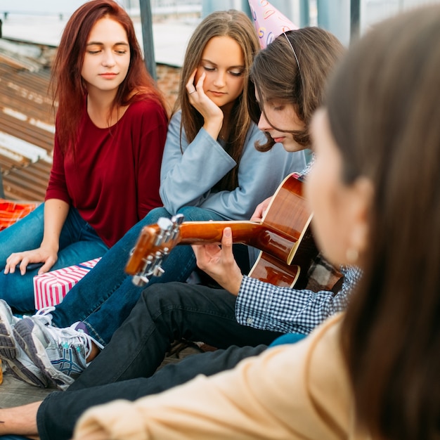Les filles écoutent un garçon qui joue de la guitare. Art de la musique style de vie. Sons captivants d'une performance romantique
