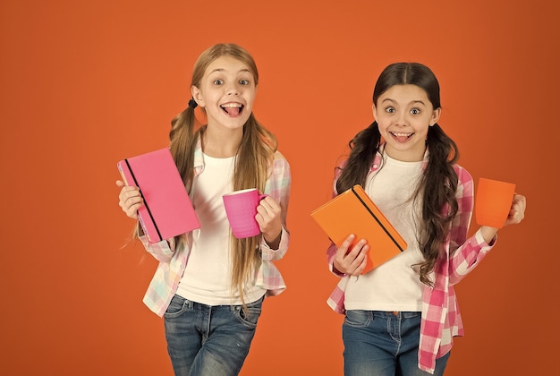 Filles enfants avec des livres et des tasses à thé fond orange Les amis passent des loisirs à lire des livres Avoir une pause se détendre Boire du thé en lisant un livre Sœurs se détendre avec une boisson Lire une activité agréable