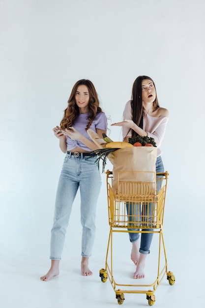 filles excitées avec sac à provisions assis dans le panier, isolées sur blanc