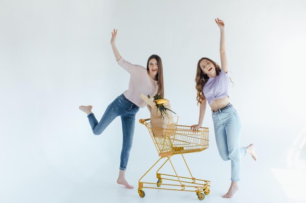 filles excitées avec sac à provisions assis dans le panier, isolées sur blanc