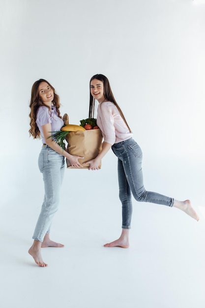 filles excitées avec sac à provisions assis dans le panier, isolées sur blanc