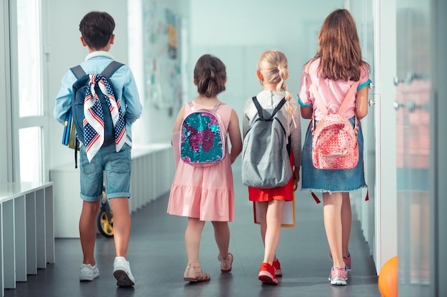 Filles et garçon portant de beaux sacs à dos lumineux allant à la leçon