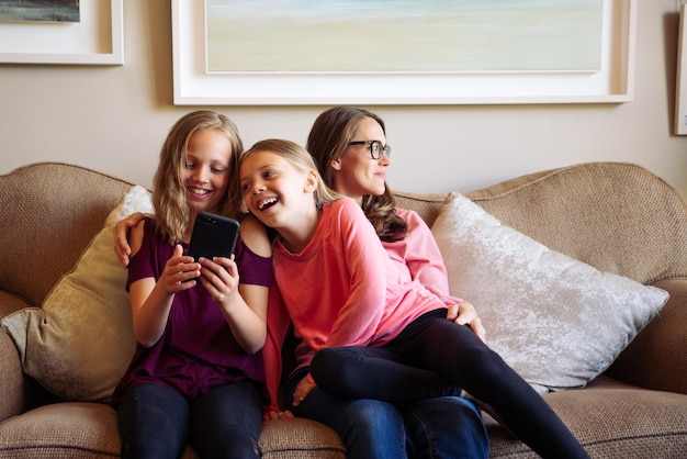 Des filles heureuses qui utilisent leur téléphone assises sur le canapé.