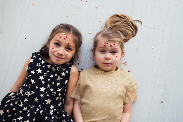 filles heureuses s'amusant le temps de noël allongées sur le sol avec des confettis brillants