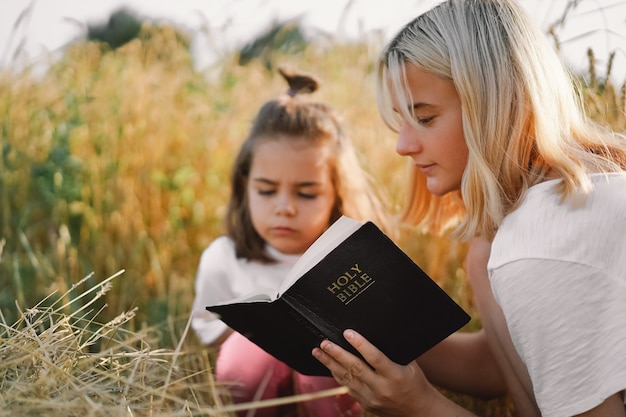 Filles lisant la Sainte Bible dans un champ de blé. Étudiez ensemble la sainte bible.