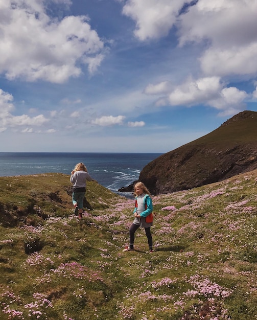 Photo des filles marchant sur les montagnes par la mer contre un ciel nuageux