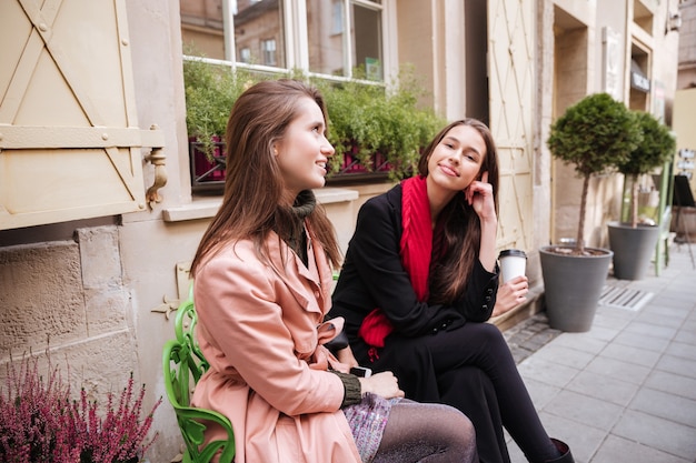 Les filles de la mode en manteaux sont assises dans la rue