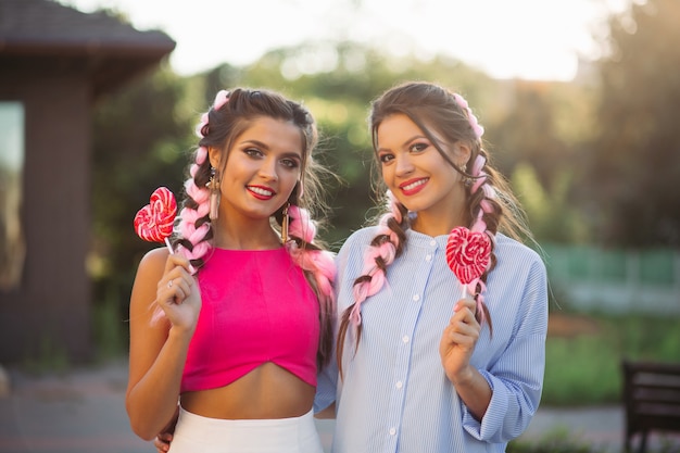 Filles à la mode avec des tresses colorées avec des bonbons coeur sur bâton.