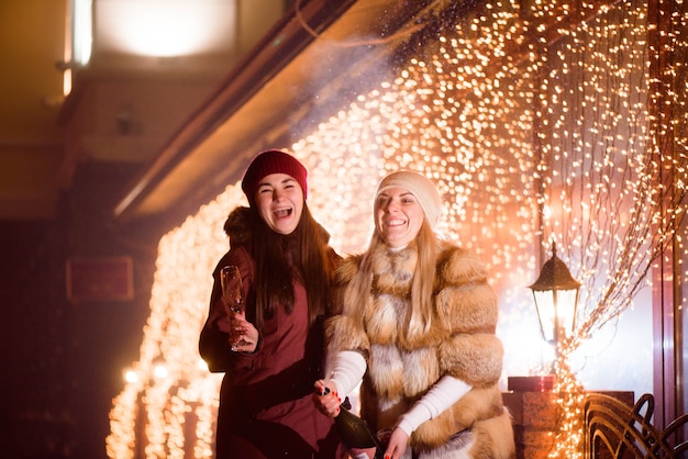 Filles riantes gaies célébrant la fête avec du champagne à l'extérieur.