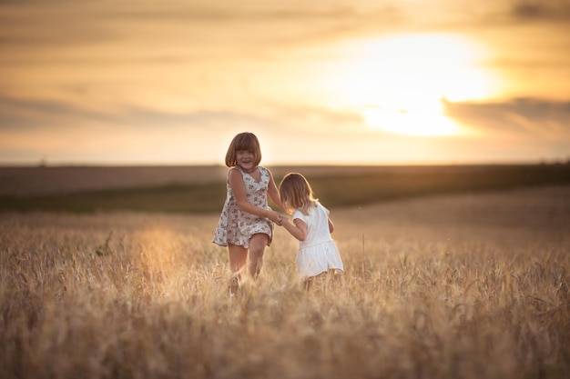 Filles sœurs marchent dans le champ avec le coucher du soleil de seigle