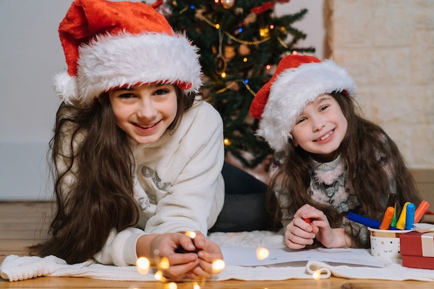 Filles souriantes en bonnet de Noel écrivant une lettre pour des cadeaux au père Noël.