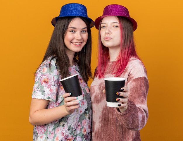 Filles souriantes portant un chapeau de fête tenant une tasse de café à la caméra