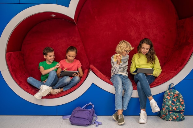 Filles avec tablettes et garçons se reposant dans la zone lounge