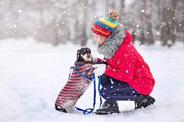 Des filles vêtues de vestes chaudes et de chapeaux jouent dans un parc d'hiver avec un chien en promenade