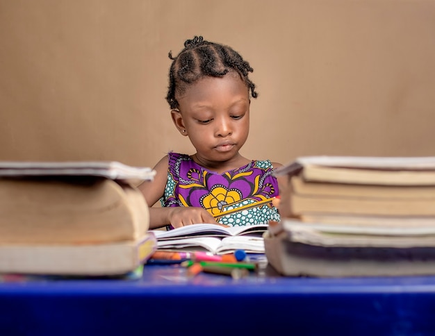 Photo une fillette africaine étudie seule avec des livres sur sa table en vue de l'examen