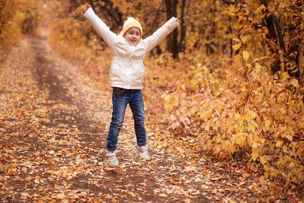 Une fillette d'âge préscolaire traverse joyeusement la forêt colorée d'automne. Le concept de repos dans la forêt en automne.