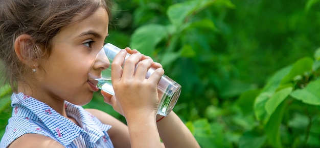 Une fillette boit de l'eau dans un verre. Mise au point sélective. Enfant.