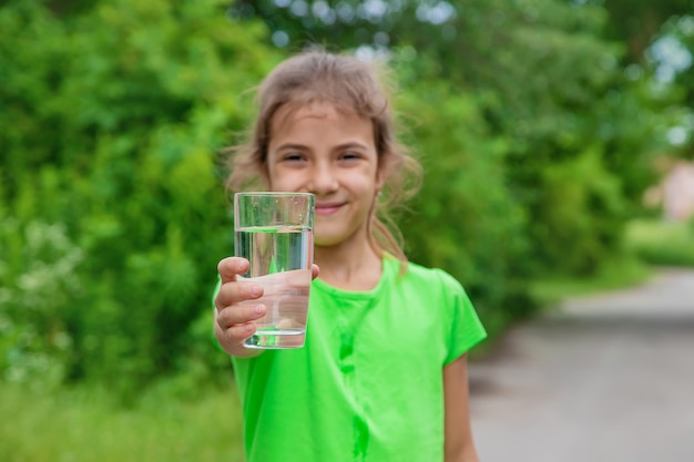 Une fillette boit de l'eau dans un verre. Mise au point sélective. Enfant.