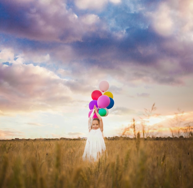 Une fillette de cinq ans tient des ballons dans une main, debout à l'extérieur sur le terrain. Concept de liberté et d'inspiration