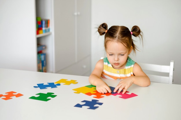 Une fillette de deux ans collectionne des puzzles assis à une table dans la pépinière