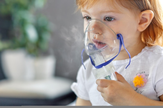 Une fillette de deux ans tient un masque inhalateur et respire un concept de traitement contre la toux