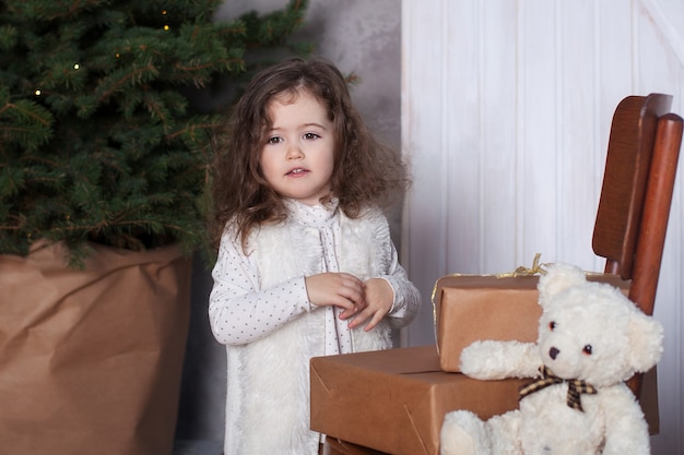 Une fillette se tient à côté de cadeaux sur une chaise à Noël dans le salon