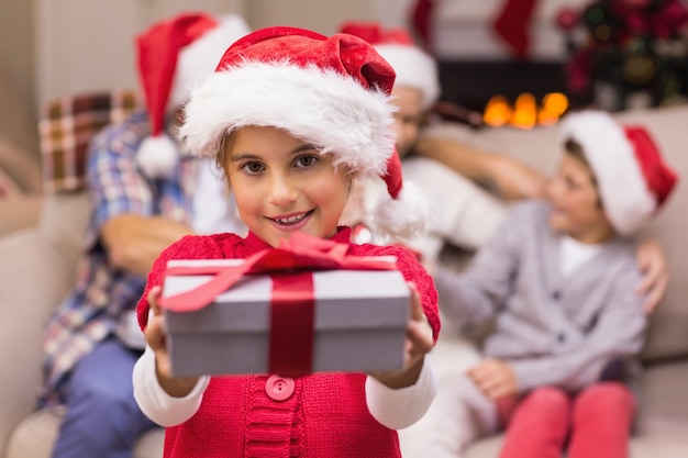 Fillette souriante offrant un cadeau avec ses parents derrière