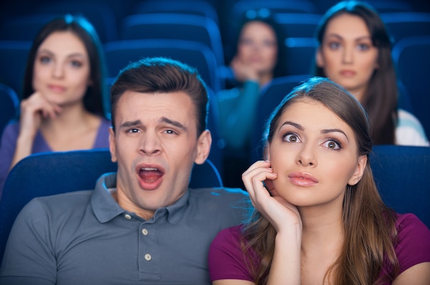 Film ennuyeux ? Jeune homme ennuyé assis près de sa femme excitée en regardant un film au cinéma