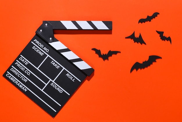 Film d'horreur, thème d'halloween. Clap de cinéma et chauves-souris décoratives volantes sur orange vif