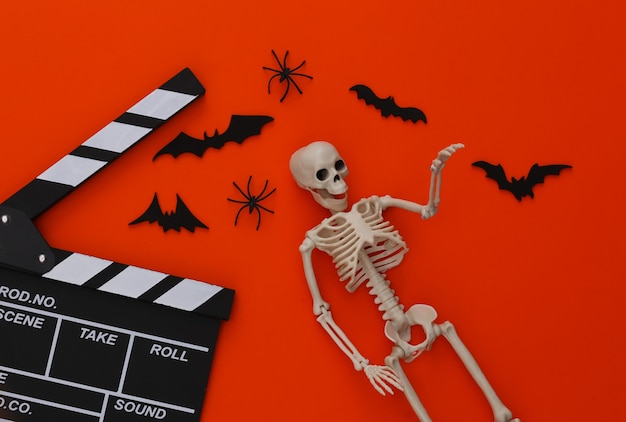 Film d'horreur, thème d'halloween. Clap de cinéma, squelette, araignées et chauves-souris décoratives volantes sur orange