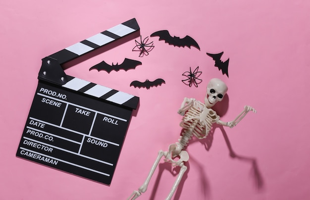 Film d'horreur, thème d'halloween. Clap de cinéma, squelette, araignées et chauves-souris décoratives volantes sur rose vif