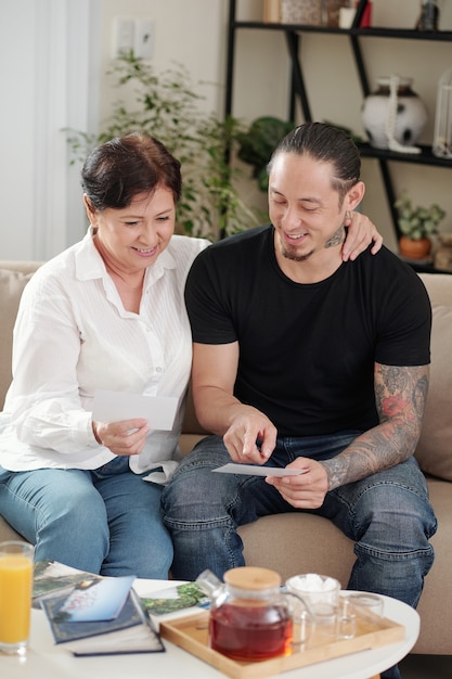 Fils aîné assis avec sa mère sur le canapé et regardant les photos de l'album pendant qu'ils boivent du thé