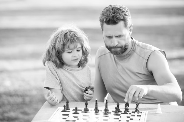 Fils allongé sur l'herbe et jouant aux échecs avec le père enfant garçon concentré développant la stratégie d'échecs pla