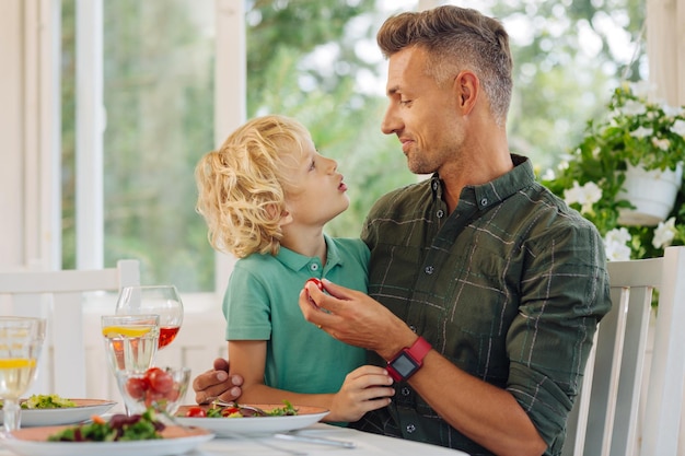 Fils aux cheveux blonds bouclés parlant avec papa tout en déjeunant