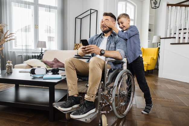 Fils couvrant les yeux d'un père handicapé dans un salon moderne