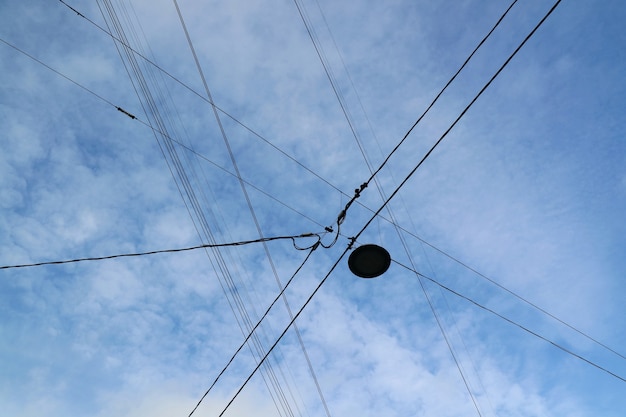 Fils électriques avec lampadaire contre ciel bleu et nuage blanc.