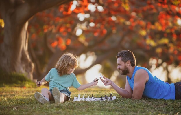 Fils enfant portant sur l'herbe et jouant aux échecs avec le père