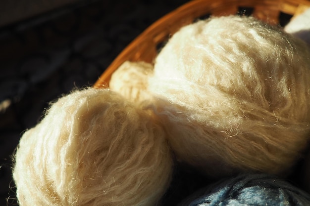 Fils de laine et d'acrylique blanc beige et bleu enroulés en pelote ou en écheveau Plusieurs écheveaux de laine légère dans un panier Le tricot comme passe-temps Un bout de fil