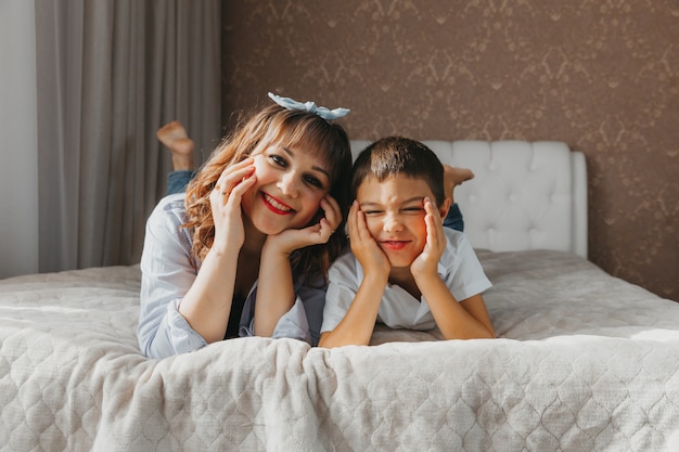 Le fils et la maman heureux s'allongent sur le lit et rient. Fête des mères!