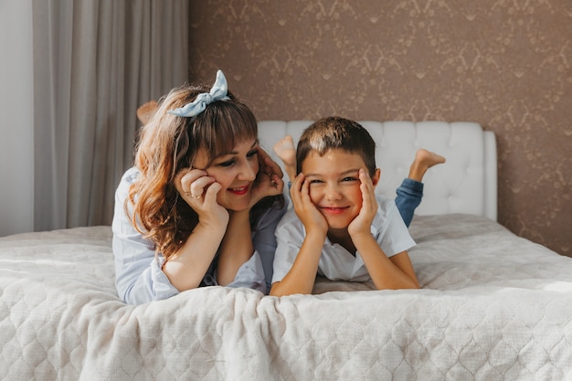 Le fils et la maman heureux s'allongent sur le lit et rient. Fête des mères!