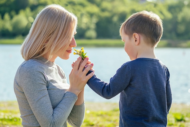 Le fils mignon de bébé donne des fleurs de cadeau à sa belle mère blonde en parc sur un fond d'herbe verte. concept de fête des mères.