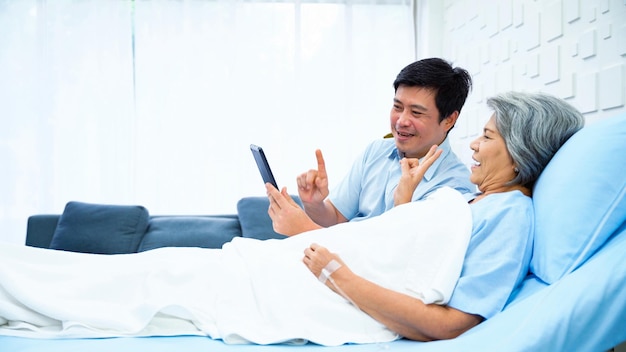 Photo fils d'une patiente âgée utilisant une tablette pour enregistrer une vidéo pendant que sa mère est allongée dans son lit