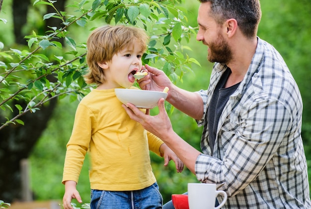 Fils et père mangeant en plein air. Petit déjeuner le matin. Nourriture savoureuse. alimentation saine et régime. Les produits laitiers. joyeuse fête des Pères. Petit garçon avec papa mange des céréales. temps de repos en famille. Week-end en famille.