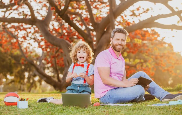 Fils avec père regardant la leçon sur ordinateur portable à l'extérieur de l'éducation en plein air