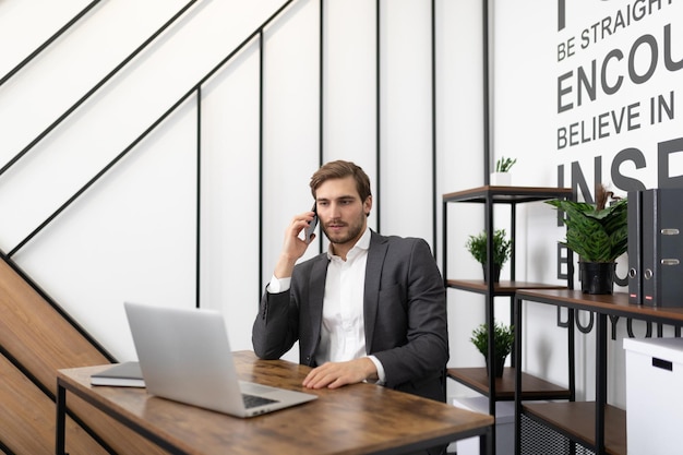 Financier masculin assis à table avec un ordinateur portable et faisant des appels à chaud