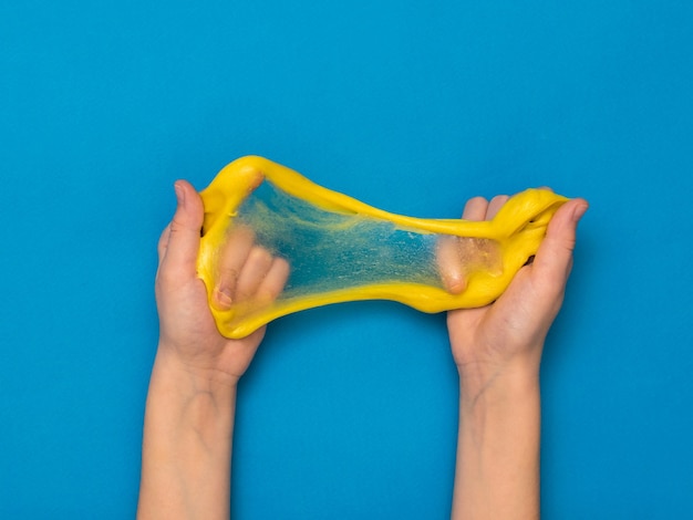 Une fine pellicule de bave jaune dans les mains d'un enfant sur fond bleu. Jouet antistress. Jouet pour le développement de la motricité de la main.